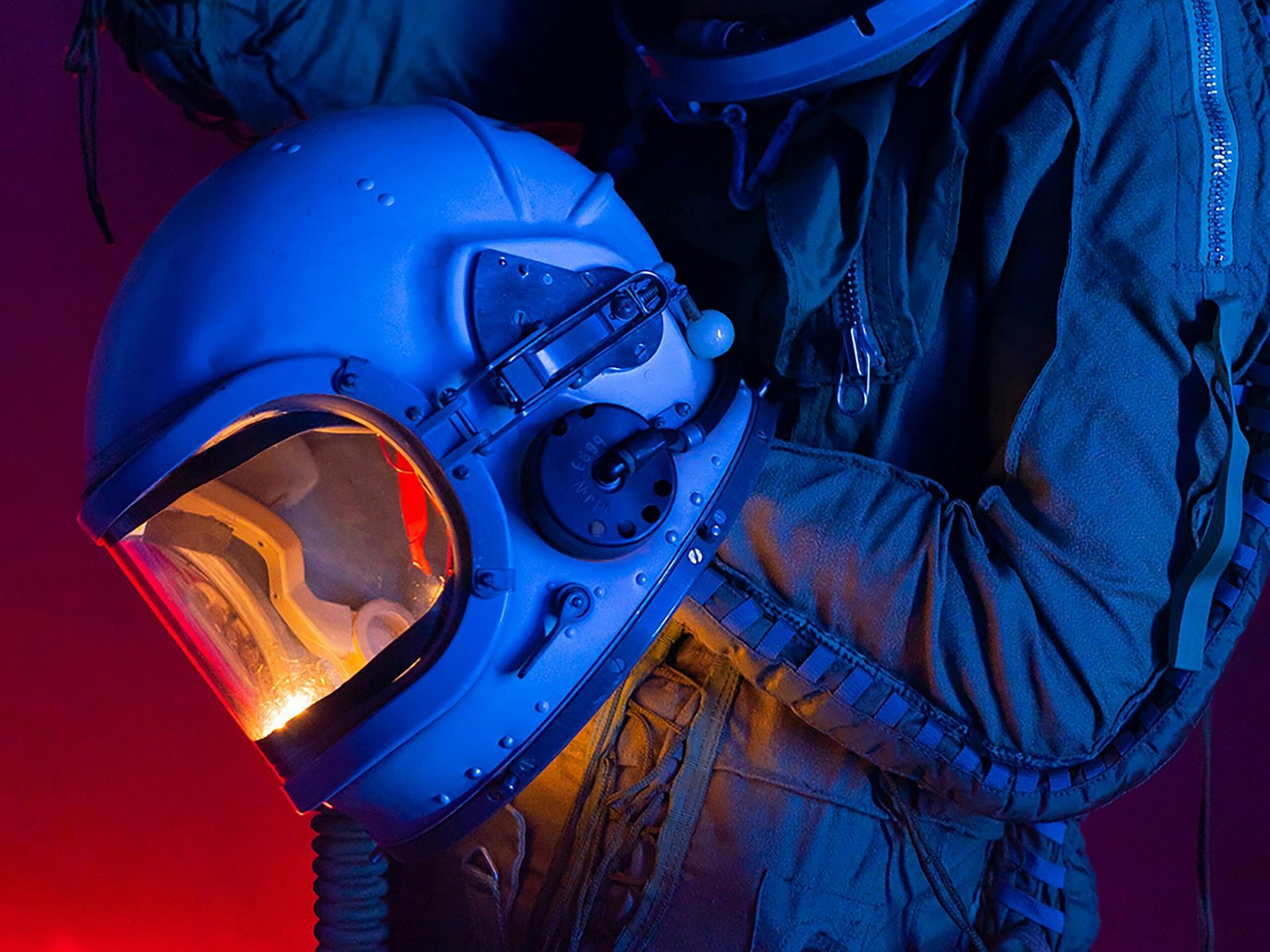 A person in a spacesuit holding an astronaut helmet with colorful lighting.
